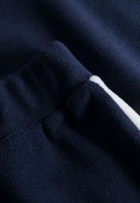 Marineblaue Stoff mit einer weichen, flauschigen Textur. Verfügt über einen weißen Akzent und einen gerafften Taillenbund. Nahaufnahme, die die Struktur des Materials zeigt.