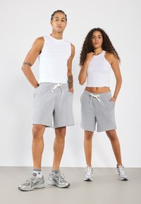 Deux personnes portant des débardeurs blancs ajustés et des shorts d'athlétisme gris avec des ceintures élastiques et des lacets, associés à des baskets.