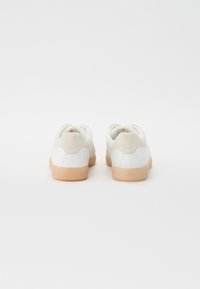 Sneakers bianchi con tomaia in pelle e dettagli in suede, suola in gomma e design della punta arrotondata, presentati da una vista posteriore.