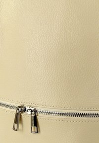 Gros plan sur du cuir beige texturé avec une fermeture éclair argentée horizontale dotée de deux tirettes rectangulaires.