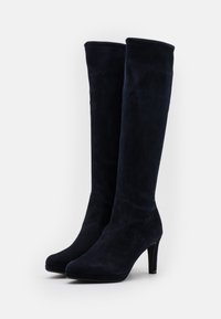 Bottes hautes jusqu'au genou en daim bleu marine avec des bouts pointus, une silhouette élégante et des talons hauts. Texture lisse avec un minimum de détails.
