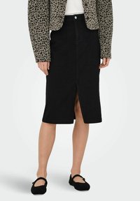 Falda de mezclilla negra con una abertura en el frente, que presenta un diseño clásico y un corte de longitud media. Combinada con una chaqueta de estampado de leopardo y bailarinas negras.