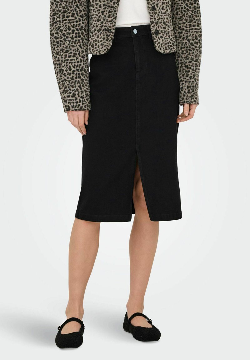 Falda de mezclilla negra con una abertura en el frente, que presenta un diseño clásico y un corte de longitud media. Combinada con una chaqueta de estampado de leopardo y bailarinas negras.