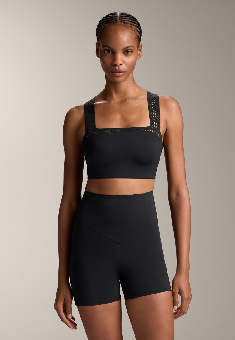 Black activewear set featuring a square-neck sports bra with perforated straps and high-waisted shorts. Smooth, stretch material.