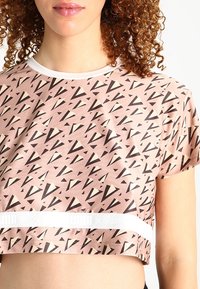 Top corto rosa con patrones triangulares en negro y crema. Hecho de una tela suave, cuenta con una banda blanca con el logotipo "PUMA x Nature".