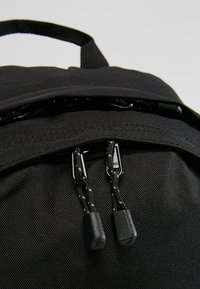 Zaino nero caratterizzato da un tessuto testurizzato, due scomparti con zip dotati di cursori neri e una maniglia superiore rinforzata per il trasporto.