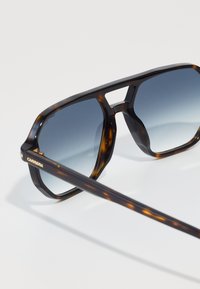Occhiali da sole tartaruga marrone con lenti grigie sfumate, forma rettangolare, montatura spessa e marchio "CARRERA" in oro sul lato.
