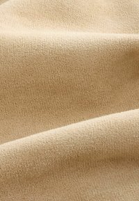 Tissu doux beige avec une surface texturée, légèrement duveteuse et des plis doux créant des ombres subtiles.