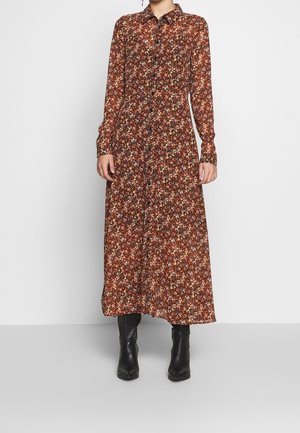Długa sukienka kwiatowa w kolorze brązowym z zapinanym na guziki kołnierzem, z wzorem małych kolorowych kwiatów i długimi rękawami. Czarny buty dopełniają stylizację.