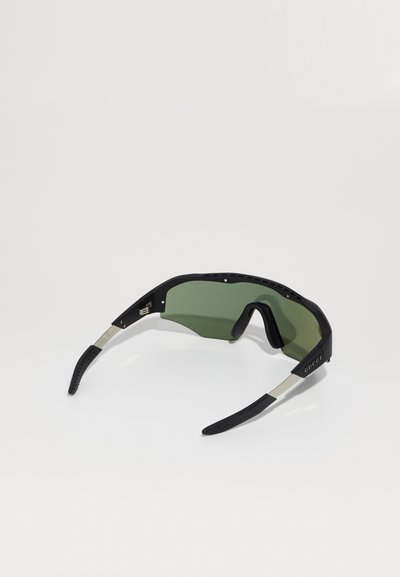 Óculos de sol pretos com lentes verdes; o design desportivo apresenta formas angulares, armação emborrachada e detalhes metálicos nas hastes.