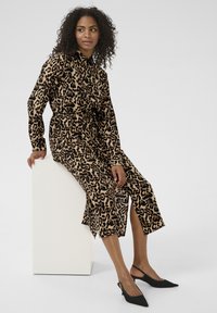 Abito a fantasia leopardata in beige e nero, maniche lunghe, chiusura a bottoni frontale, vita definita e spacchi laterali; abbinato a décolleté nei toni del nero.