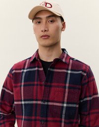Rød og marineblå ternet flannel skjorte med knaplukning og lomme, sammen med en beige baseballkasket med rødt skrift.