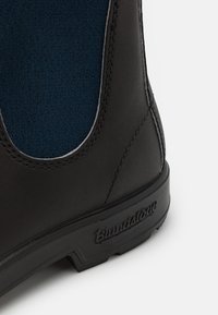 Botín de cuero negro con panel lateral de elastano azul, detalle de costuras grises y suela de goma texturizada con la marca embellecida.