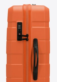 Oranžový tvrdý kufr s texturovaným povrchem, černým zipovým zámkem, číselným kombinovaným ciferníkem a bočním madlem pro snadné nošení.