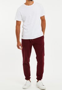 Witte katoenen T-shirt met ronde hals, gecombineerd met bordeaux fleece joggers met elastische boorden en witte veterschoenen.