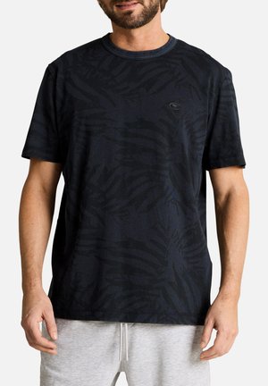 Mann trägt ein schwarzes kurzärmliges T-Shirt mit dezentem Blattmuster und hellgraue Shorts mit Kordelzug vor weißem Hintergrund.