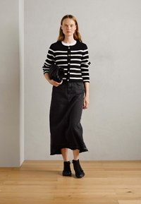 Cardigan a righe bianche e nere con bottoni, abbinato a una gonna di jeans nera. Stivali neri alla caviglia e una clutch nera completano l'outfit.