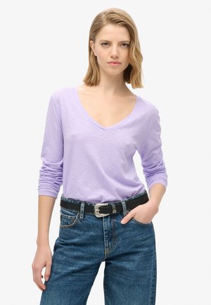 Lys lavendel langærmet skjorte med V-hals design, parret med højhalsede blå jeans og et sort bælte med en sølvspænde.