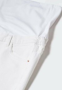 Camiseta de algodón blanca doblada sobre unos pantalones vaqueros blancos con un bolsillo trasero y un pequeño acento en rosa dorado en la costura del bolsillo. Textura suave.