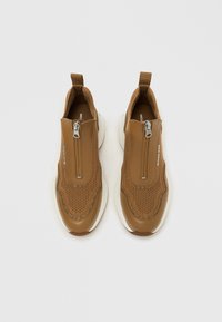 Rjavi natikači z izboljšanim zgornjim delom z mrežastimi detajli, z zapiranjem na zadrgo in belim podplatom s zaobljenim dizajnom.