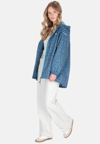 Blå leopardmönstrad jacka med huva, med elastiska muddar och dragsko, kombinerad med ljusa jeans och vita sneakers.