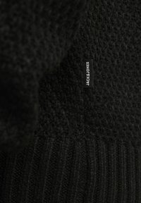 Schwarzer gestrickter Pullover mit strukturiertem Muster und geripptem Saum. Mit einem kleinen Markenschild "JACK & JONES", das am Stoff befestigt ist.
