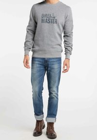 Felpa grigia con stampa "Drei & Master", maniche lunghe, polsini e orlo a coste. Abbinata a jeans di denim e stivali marroni con lacci.