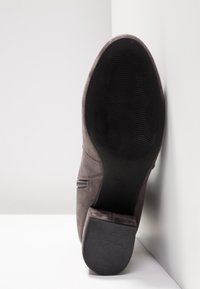 Botte en daim gris foncé positionnée verticalement avec semelle noire texturée et talon bloc visibles, sur fond blanc en coin.