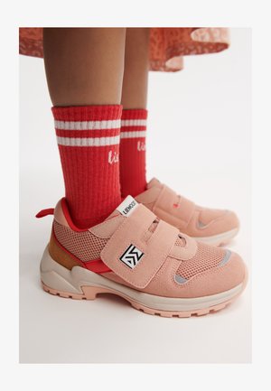 Rosa treningst sneakers med mesh- og semsket skinnmateriale, med borrelåsrem, logopatch og en teksturert beige såle. Røde ankelsokker med hvite striper.
