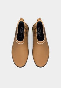 Ζευγάρι καφέ ankle boots Chelsea με μαύρες σόλες και λογότυπο Barbour στο μπροστινό μέρος και εσωτερικά, φωτογραφημένα από πάνω σε λευκό φόντο.