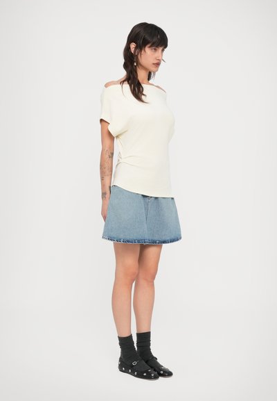 Ανοιχτό κίτρινο T-shirt με άνετη εφαρμογή και λαιμόκοψη που αφήνει τους ώμους ακάλυπτους, συνδυασμένο με μπλε τζιν φούστα με ξεβαμμένες άκρες, φορεμένο με σκούρες κάλτσες και μαύρα μπαλαρίνες.