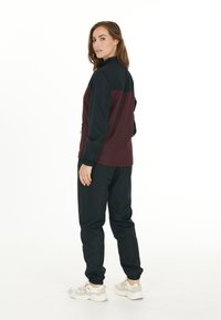 Conjunto de ropa deportiva que incluye una chaqueta bloqueada en colores marino y burdeos con cuello alto y pantalones con puños elásticos, fabricados en material liviano.