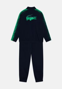 Survêtement marine avec un dégradé de vert sur les manches, une taille élastique et un logo de crocodile imprimé au dos. Texture de tissu lisse.