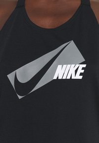 Czarny top na ramiączkach z dużym szarym logo Nike oraz słowem "NIKE" w pogrubionej białej czcionce, oba umieszczone w geometralnym wzorze.