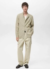 Camicia crinkled color oliva chiaro con colletto aperto, abbinata a pantaloni cargo beige con tasche laterali. Sandali neri con cinturini completano l'outfit.