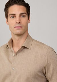 Beige linnen shirt met een klassieke kraag, eenknops sluiting en een gestructureerde stof. Kenmerkt zich door een subtiele, lichte weving.