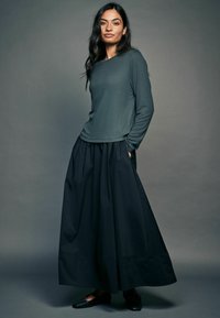 Langærmet, mørkegrøn struktureret top parret med en højtaljeret, svævende sort nederdel. Sorte flade sko fuldender outfittet.