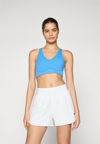Top desportivo azul com um design de decote em V e costura de suporte, combinado com calções brancos que apresentam um cós elástico e bolsos laterais.