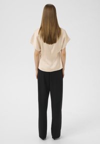 Haut en satin beige avec des manches courtes et larges, associé à un pantalon noir ample. Texture lisse et design cintré visibles de l'arrière.