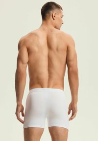 Białe bawełniane bokserki z płaskim pasem ze subtelnie wytłoczonym logo. Gładka faktura, długość do połowy uda i dopasowany krój.