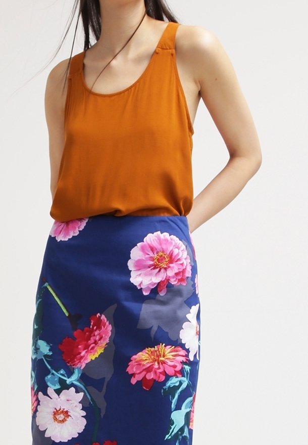 Top senza maniche marrone abbinato a una gonna blu aderente a fiori caratterizzata da grandi fiori rosa e bianchi, che mette in mostra colori vivaci e dettagliati motivi.
