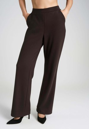 Pantaloni ampi di colore marrone scuro con una texture liscia, vita alta e tasche laterali. Abbinati a tacchi alti neri a punta.