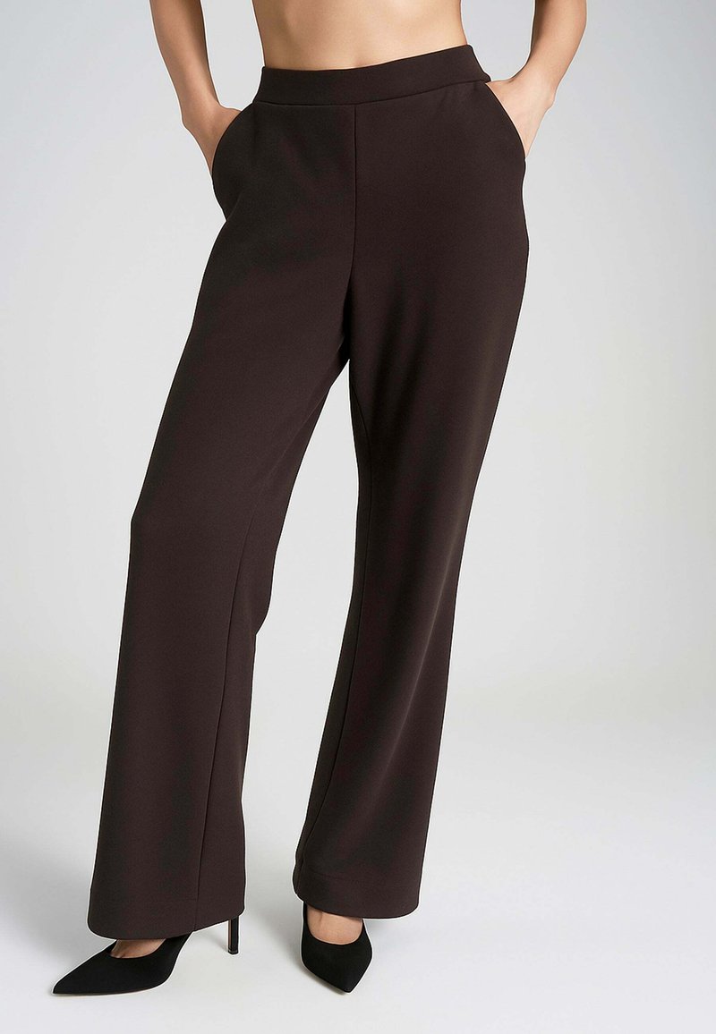 Pantaloni ampi di colore marrone scuro con una texture liscia, vita alta e tasche laterali. Abbinati a tacchi alti neri a punta.