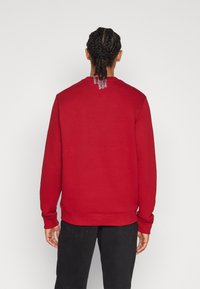Sudadera roja hecha de un tejido suave, con cuello redondo, puños acanalados y un acento único en la parte posterior cerca del cuello.