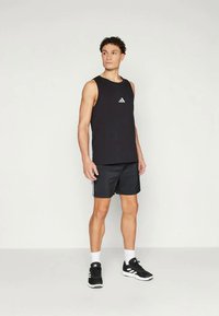 Top de alças preto sem mangas com o logótipo branco da Adidas, combinado com calções pretos com riscas brancas laterais e sapatos de desporto pretos.