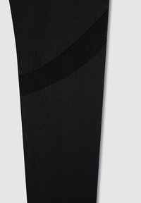 Czarne legginsy sportowe z gładkiego materiału, z detalem w postaci siateczkowego pasa w teksturze wzdłuż linii ukośnej.