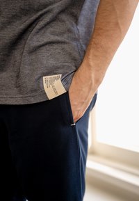 Grijze t-shirt met een zijlabel, gecombineerd met donkerblauwe broek. De t-shirt heeft een zachte textuur en de broek heeft een lichte glans.