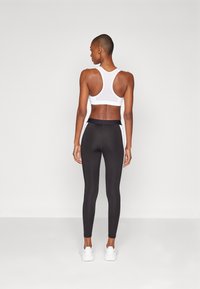 Reggiseno sportivo bianco e leggings neri, con vita alta e strisce laterali bianche, realizzati in tessuto elasticizzato. Texture liscia.