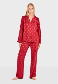 Conjunto de pijama de satén rojo que incluye una camisa de botón con un bolsillo y pantalones largos, ambos decorados con grandes y llamativos patrones de lunares.