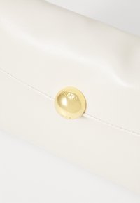 Bílá kožená peněženka s hladkým povrchem, která se uzavírá zlatým kulatým knoflíkem s vyraženým nápisem "Furla." Design je elegantní a minimalistický.